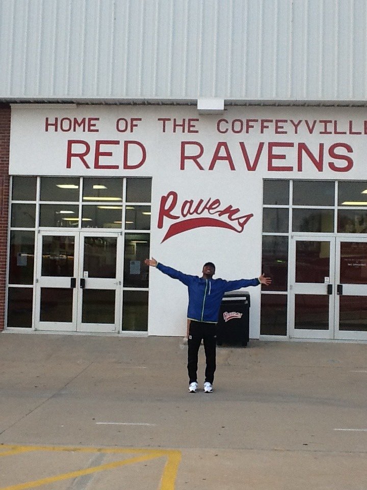 Duan Asemota, arms outstretched, in front of the Home of the Coffeyville Red Ravens facility