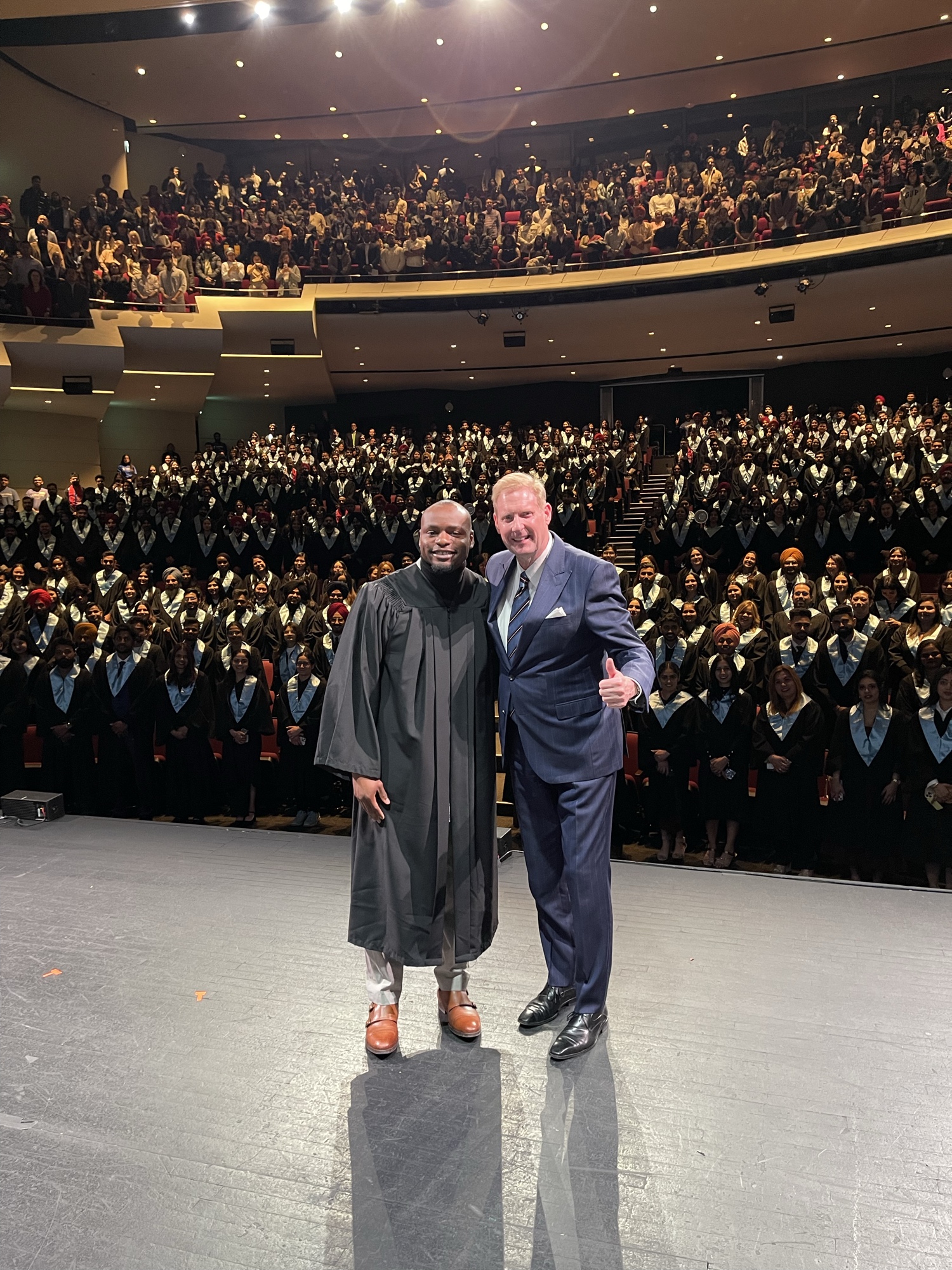 Duan Asemota on stage with the Lambton College Toronto president in front of a packed auditorium of graduating students