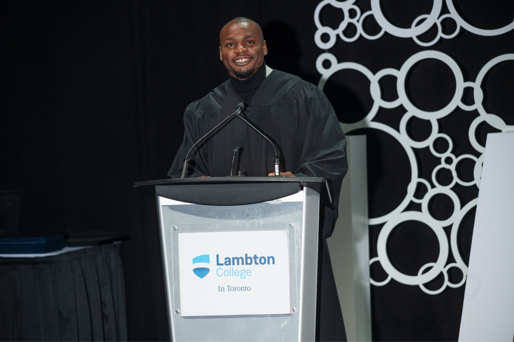 Duan Asemota in a black academic robe at the Lambton College Toronto convocation podium
