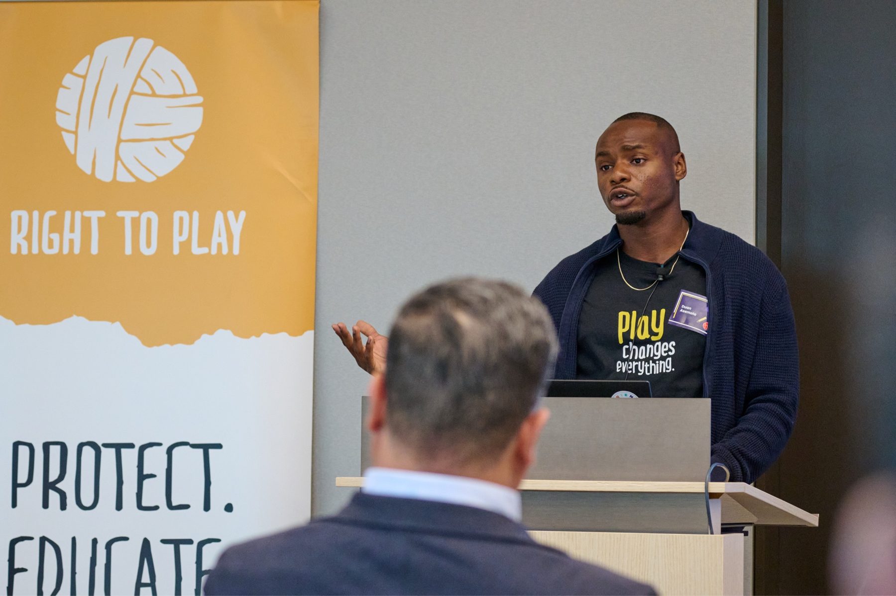 Duan Asemota speaking at a Right To Play banner